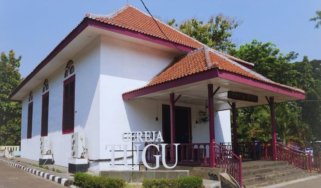 Whatsapp image 20260612 at 19 38 55 catrawarta Small white church with a red tiled roof purple trim and a front veranda labeled gereja tugu